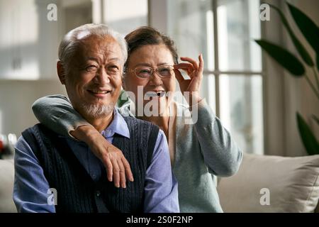 portrait of a happy senior asian couple sitting on couch looking at camera smiling Stock Photo