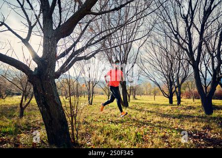 Athletic bearded man in red shirt running on trail path in autumn forest at sunrise Stock Photo