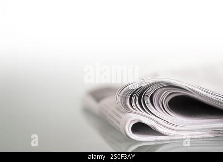 Folded newspapers mirrored on a glass table against a plain light background, narrow depth of field. Space for text on the left Stock Photo