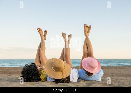 Three young women relaxing on the beach with legs up Stock Photo