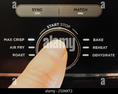 Macro closeup of a finger pressing a food air fryer start stop button, in the middle of various heating program options. Stock Photo