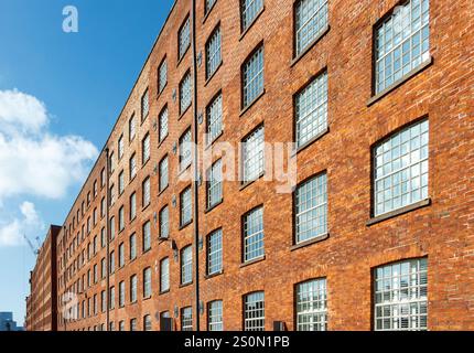 perspective view of A long row of vintage red brick factory buildings with large windows under a bright blue sky new islington manchester uk Stock Photo