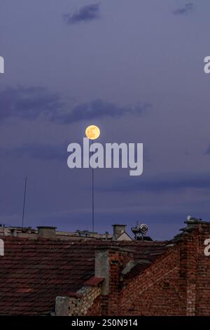 The full moon over the rooftop shines so brightly the moon is aligned with a lightning rod. Stock Photo