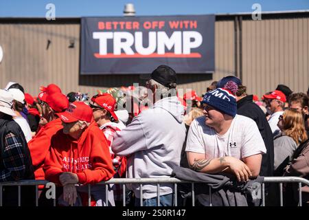 Trump supporters stand in a crowd with a large TRUMP sign hanging on a building in the background during an outdoor rally. Stock Photo