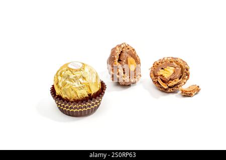 One whole Ferrero Rocher chocolate candy and one cut in half lie on a white background. A chocolate-covered nut with a gold wrapper lies on a white ba Stock Photo