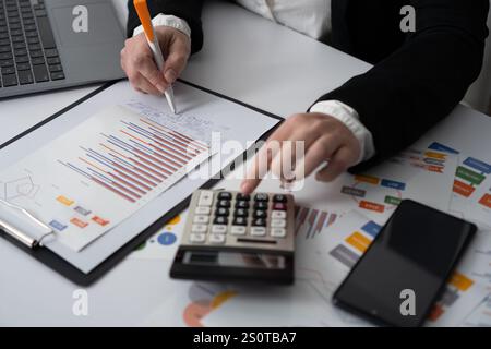 A dedicated business professional is thoroughly analyzing complex financial data using a calculator and a laptop to ensure accurate results, aiding in Stock Photo