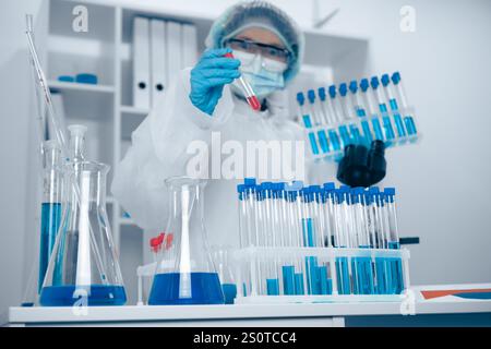 A dedicated scientist is currently working in a laboratory, meticulously analyzing blue liquid samples that are placed in various test tubes as part Stock Photo