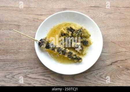 baking cherry or golden apple snail stabbing wooden stick dressing Thai spicy seafood sauce on plate Stock Photo