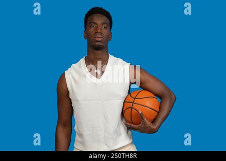 Young man wearing white shirt holding basketball on blue background Stock Photo