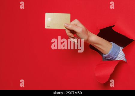 Cropped view of woman hand tearing through paper and holding credit card getting bank loan for purchase isolated on red background. Stock Photo
