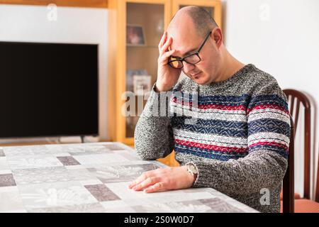 A bald adult male leaning against a table with his head resting on one of his hands and a sad look on his face. Stock Photo