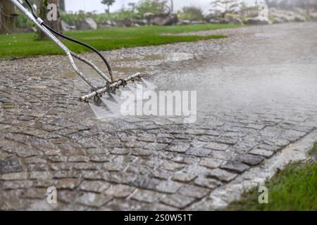 Professional cleaning service worker washing cobblestone pavement using high pressure water jet Stock Photo