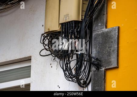A wall with a bunch of wires hanging from it. The wires are black and white. The wall is yellow Stock Photo