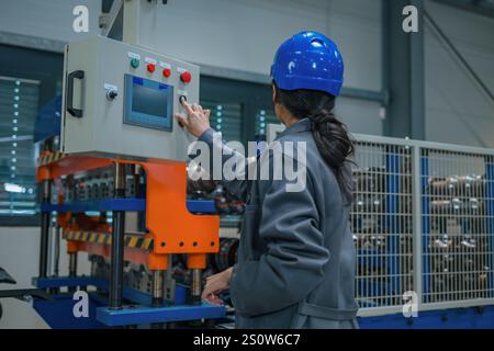 Indian woman engineer with a blue helmet and safety goggles, operating a control panel, controlling and automating industrial processes. Stock Photo