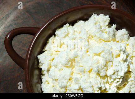 Cottage cheese in a ceramic bowl. Delicious grainy homemade cottage cheese on a ceramic background. Stock Photo