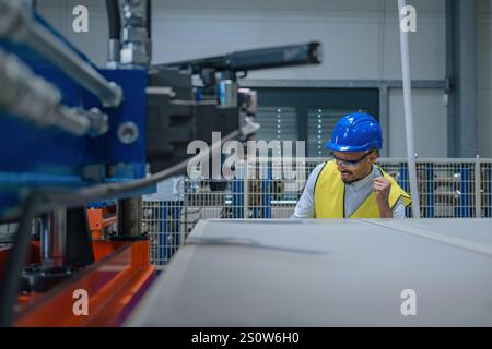 Production line engineer in a factory with yellow vest and blue helmet at work. Stock Photo