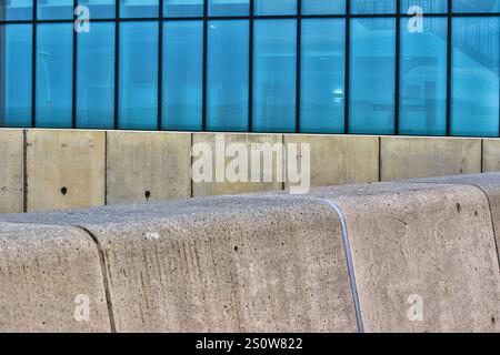 Concrete wall and blue-tinted glass facade of a modern building.  The image features a textured concrete structure in the foreground and a large panel Stock Photo