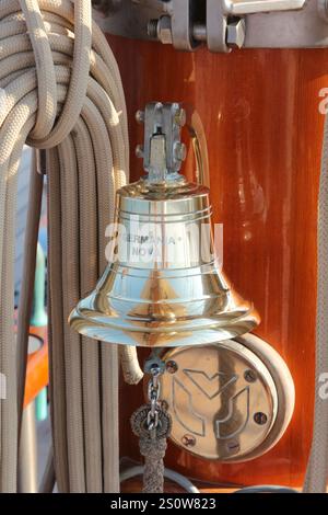 Polished Brass Ship Bell Mounted on a Wooden Mast with Nautical Ropes Stock Photo