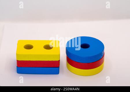 Stack of three colored wooden blocks forming a rectangular prism and a stack of three cylindrical blocks.  Primary colors are used. White background. Stock Photo