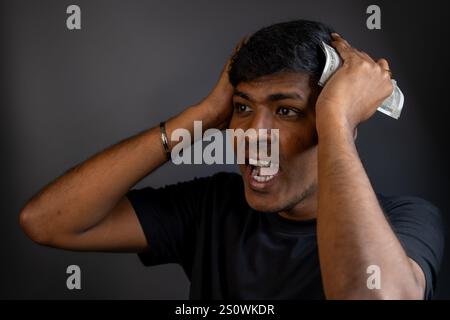 Young man stressed out over finances, holding Indian rupees. Stock Photo