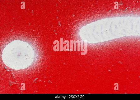 Macro close-up of a wall spray painted in bright and vibrant red with white shapes and splashes. Abstract textured splattered graffiti background. Stock Photo