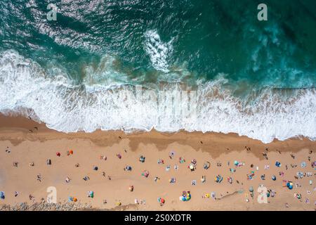 Overhead drone shot of anonymous tourist and parasols on sandy seashore. Directly above view of people enjoying summer vacations at beach during sunny day.  Stock Photo