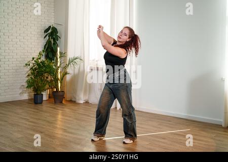 A woman is dancing in a studio with white walls and wooden floors Stock Photo