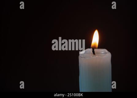 Burning ribbed pillar wax candle on the dark background with copy space. Bright flame in the darkness. Candlelight. Stock Photo