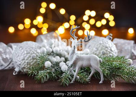 Merry Christmas and Happy New Year. White deer and christmas decorations and spruce branches on a wooden table against the background of festive light Stock Photo