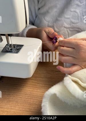 The woman cuts the thread with scissors. She is sewing a pet bed from fur fabric. Stock Photo