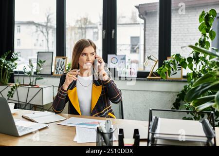 Attractive businesswoman engaged in a phone conversation in a chic, green-filled office. Stock Photo