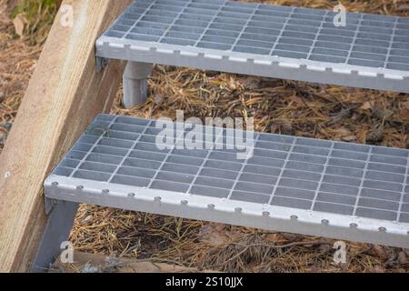 The picture shows two metal ladder steps attached to a wooden frame. The steps are made of a grid that provides good traction and are placed in a natu Stock Photo