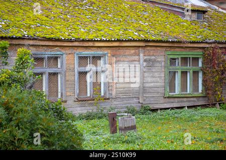 An old wooden building, the roof of which is covered with a thick layer of moss. The walls of the building are painted in different colors, but the pa Stock Photo