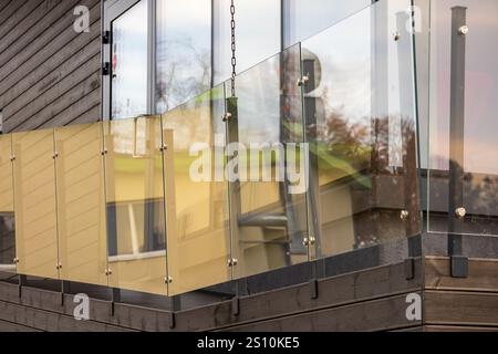 Balcony enclosed by glass balcony railings. The floor of the balcony is made of wood, and behind the glass railing you can see elements of another bui Stock Photo