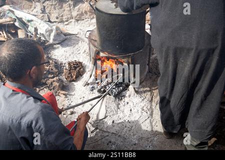 stoking wood fire boiling pot of soup or stew at traditional berber market day amazigh market asni morocco Stock Photo
