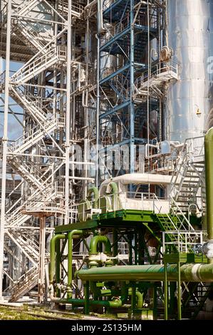 Chemical plant featuring a large distillation column with extensive metal structures and piping observed during daylight hours Stock Photo