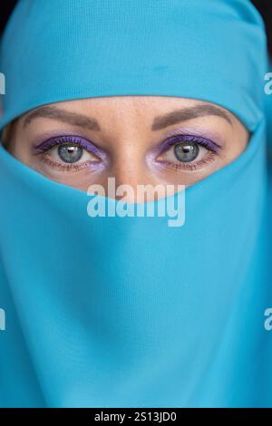 Young woman with blue eyes wearing a turquoise fabric, looking at the camera. Stock Photo