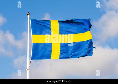 The national flag of Sweden flying in the wind at full mast against blue sky with white clouds. Stock Photo