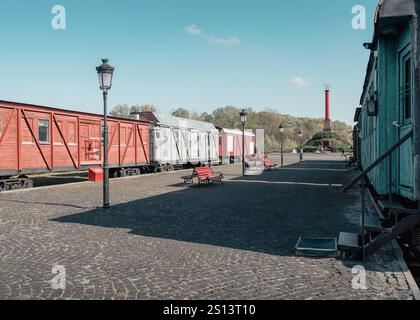 Early XX century railway station: old railcars at cobbled platform with lantern lights & benches. Kruty Heroes Memorial with column and rail platform. Stock Photo