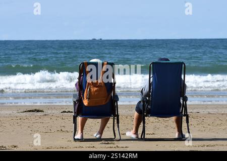 couple sitting in camping chairs on the beach looking out to sea, France, Brittany, Erquy Stock Photo