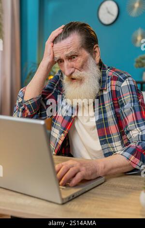 Frustrated senior mature man having software problems with laptop, angry man get nervous seeing error or mistake notification at computer screen, mad grandpa experience virus attack or app malfunction Stock Photo