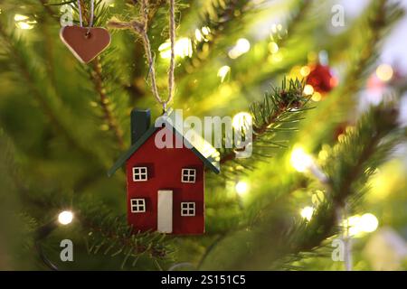 Natural, red and green house shaped ornament hanging on a Christmas tree with warm fairylights in the background Stock Photo