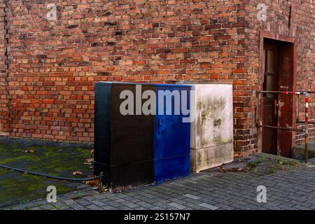 Two utility boxes with distinct colors sit against a weathered brick wall. The vibrant hues contrast with the rustic background, highlighting urban li Stock Photo
