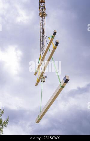 A crane lifts wooden beams into the air against a cloudy sky, illustrating construction activity Stock Photo