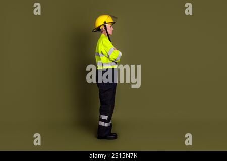 Mature female engineer in protective workwear standing confidently with arms crossed against a khaki color background Stock Photo