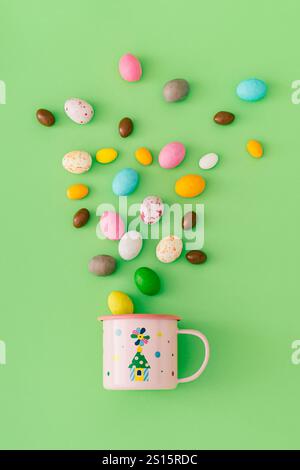 Spring composition made with colorful chocolate Easter eggs and pink mug on pastel green background. Minimal Easter concept. Stock Photo