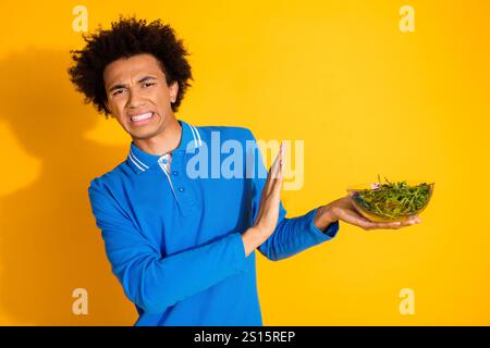 Portrait of nice young man decline salad wear blue shirt isolated on yellow color background Stock Photo