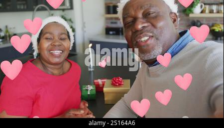 Image of pink hearts over senior african american couple in santa hats at christmas Stock Photo
