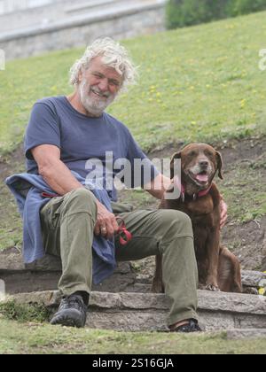 portrait of a cheerful senior man sitting on stairs with his dog at the park smiling Stock Photo