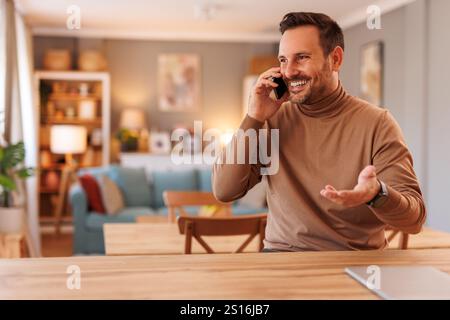 Portrait of happy male programmer discussing over smart phone while working at desk in home office Stock Photo